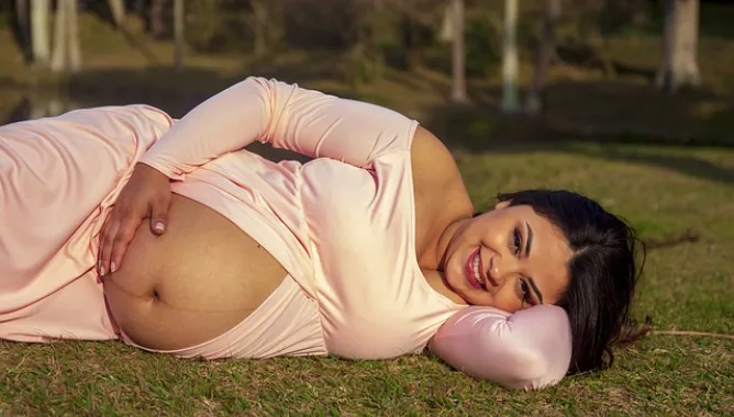 uśmiechnięta kobieta w ciąży leżąca na trawie